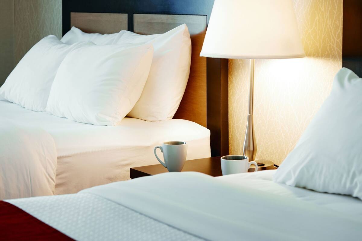 A hotel room with two beds, a nightstand with a lamp, and a cup on the nightstand.
