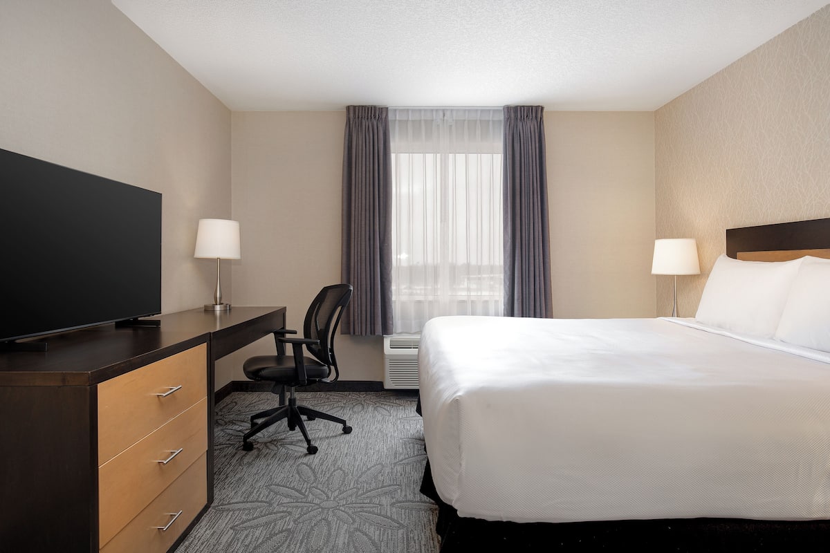 A hotel room with a bed, a desk with a chair, a television, and two lamps.