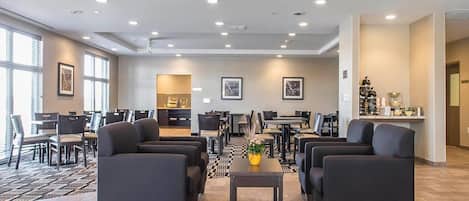 Un vestíbulo de hotel con zona de estar, mostrador de recepción y vista a la cocina.