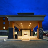 A modern hotel entrance with a covered walkway, a reception desk, and a parking area.