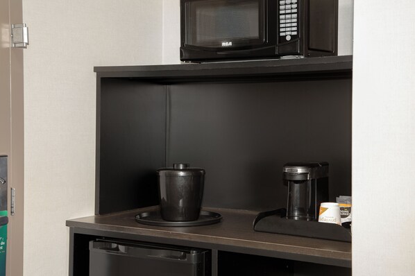 Una kitchenette con microondas, cafetera y un cesto de basura.