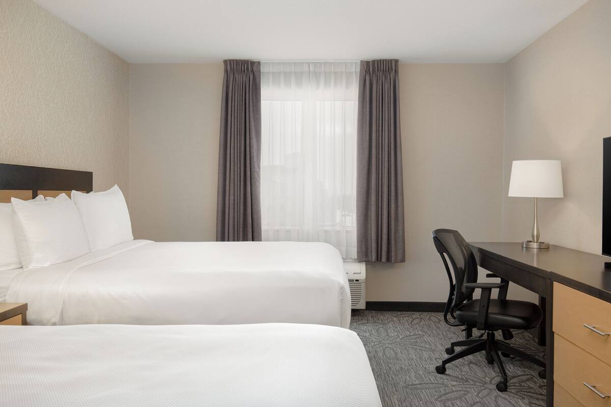 A hotel room with two beds, a desk, a chair, a lamp, and a window with curtains.
