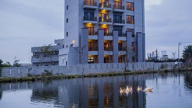 A modern multi-story hotel with balconies, located beside a calm body of water. - Flowers Bed and Breakfast (Ji'an)