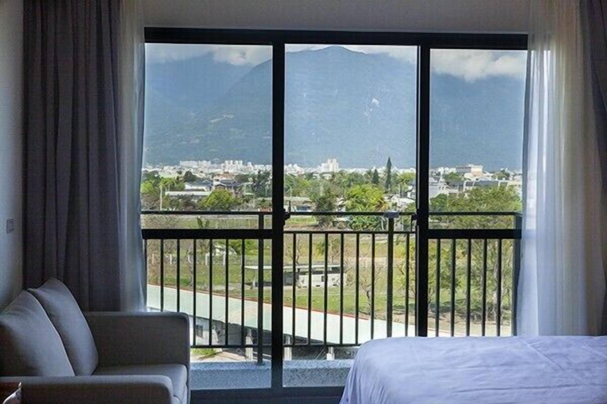 A hotel room with a large window offering a view of a cityscape and mountains.