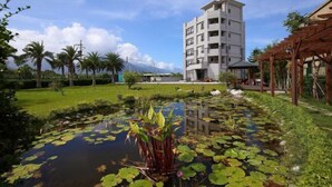 A multi-story building with a flat roof and balconies, surrounded by a well-maintained garden with a pond and lily pads. - Flowers Bed and Breakfast (Ji'an)