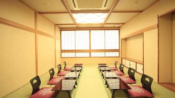 A conference room with tatami mat flooring, wooden desks, and chairs, and a large window with a grid pattern.