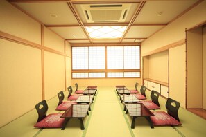 A conference room with tatami mat flooring, wooden desks, and chairs, and a large window with a grid pattern.