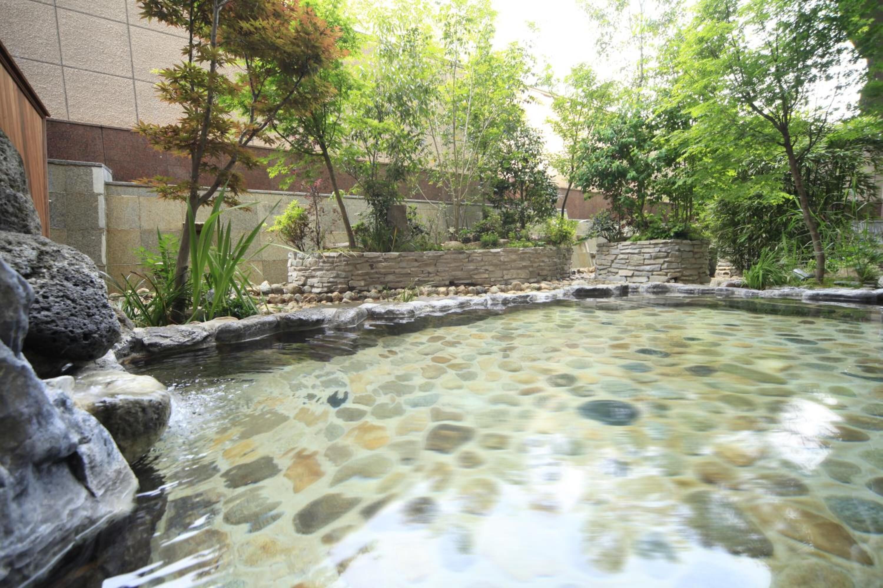 A stone-lined outdoor pool with surrounding greenery and a stone wall.