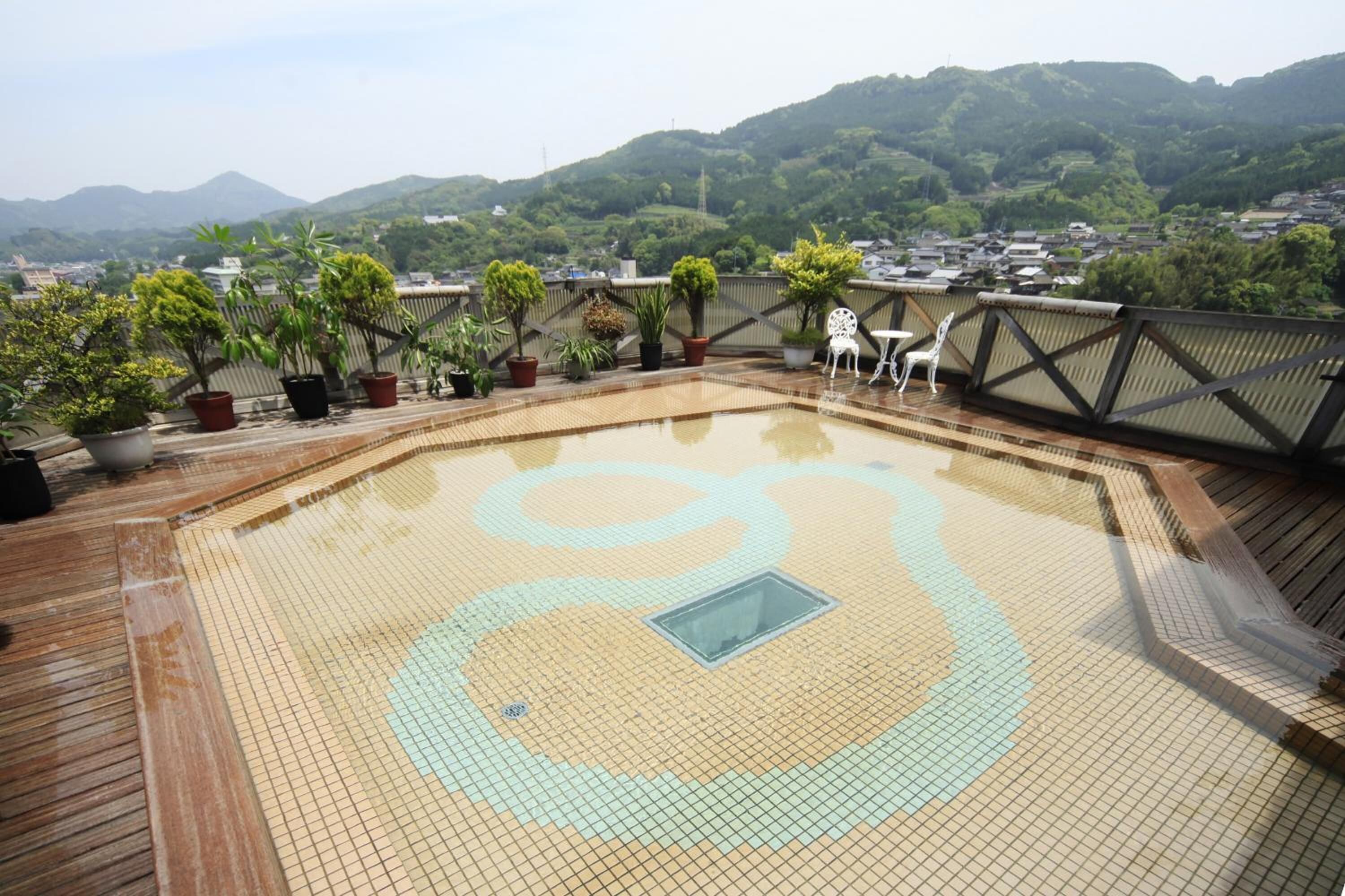 Ein Pool auf dem Dach mit einer Holzterrasse, umgeben von Topfpflanzen und Blick auf eine Stadt und Berge im Hintergrund.