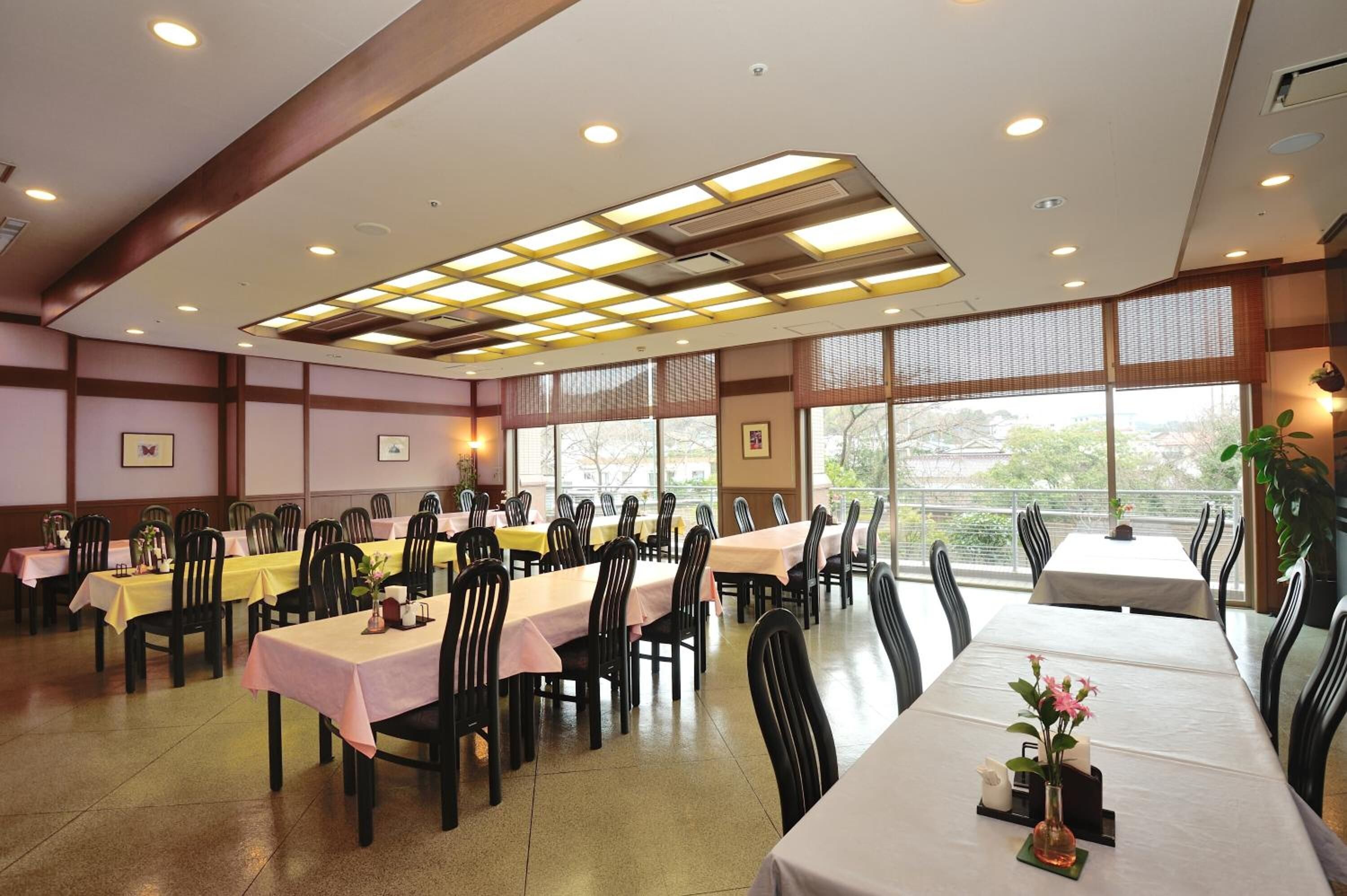 A dining area with multiple tables and chairs, large windows, and a ceiling with recessed lighting.