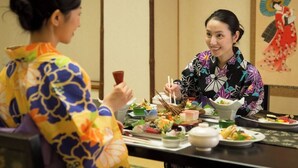 Dos personas sentadas a una mesa con varios platos, entre ellos sushi y otras comidas, en una habitación con decoración tradicional.