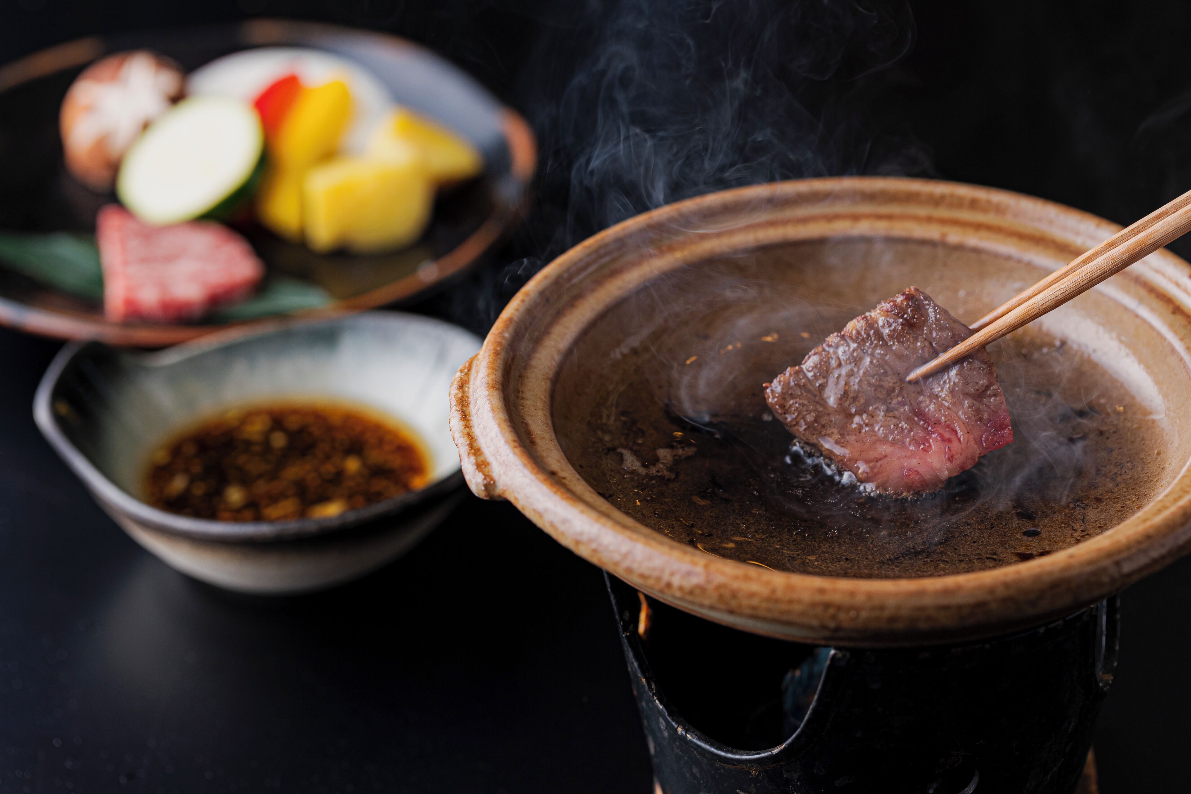 A hot pot with a piece of meat and a bowl of dipping sauce.