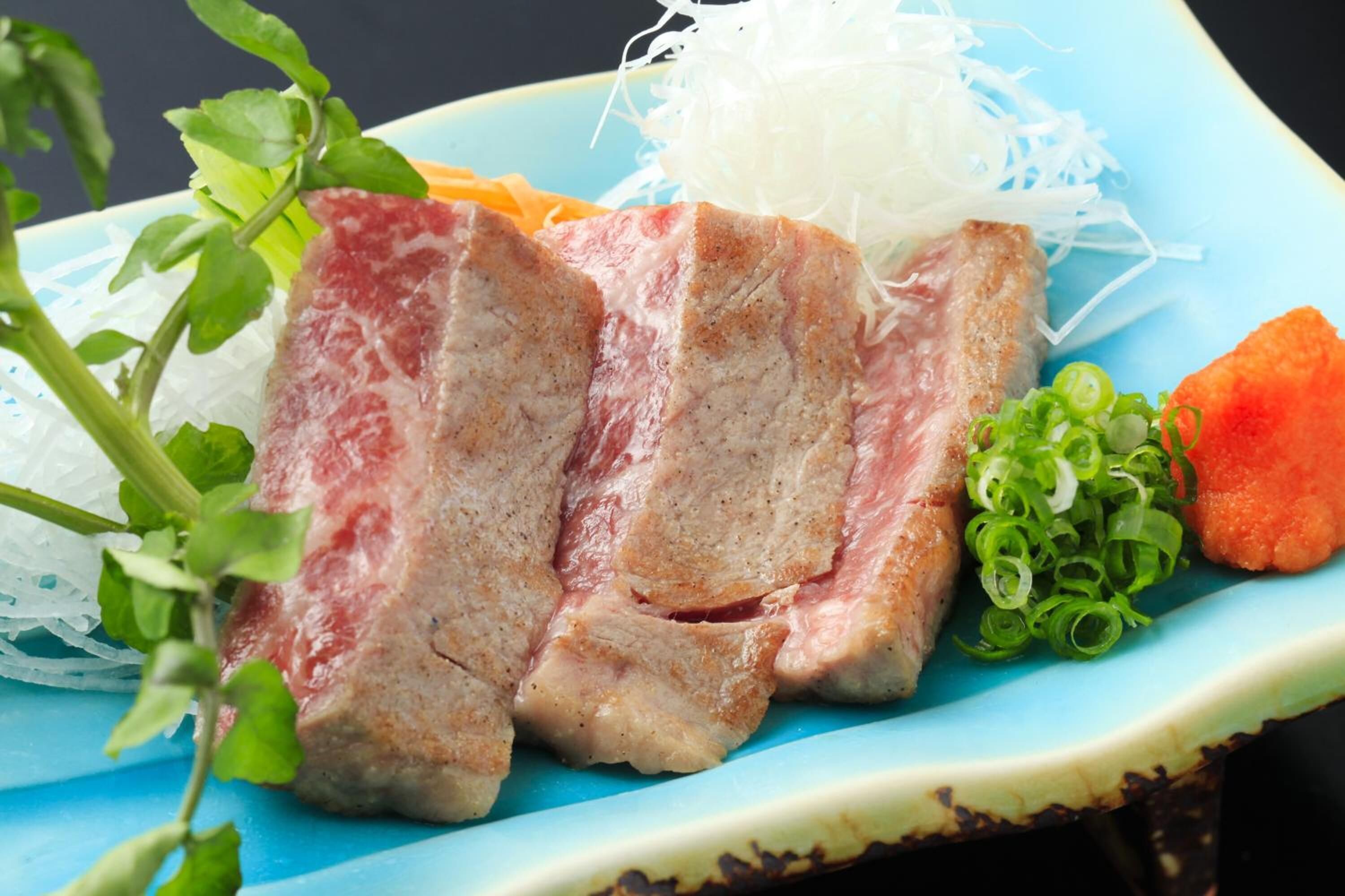 A plate with sliced meat, vegetables, and a decorative plant.