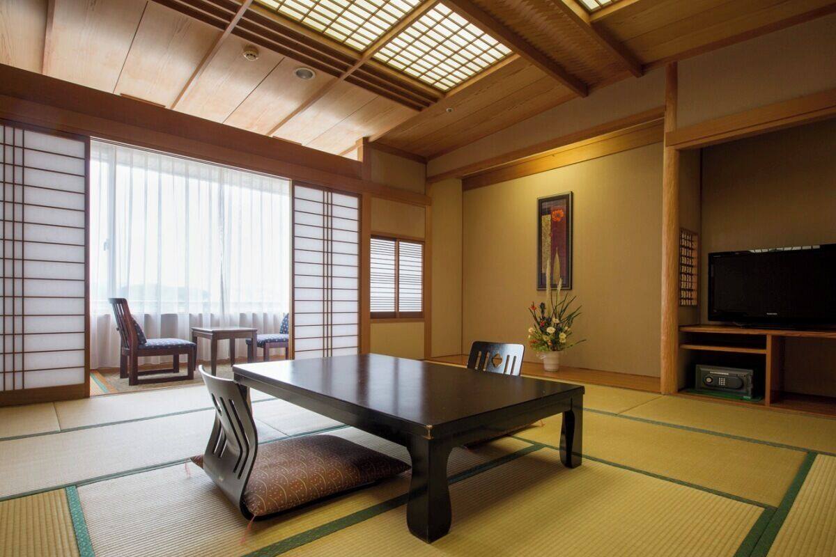 A traditional Japanese room with tatami flooring, a low table, chairs, a television, and a decorative plant.