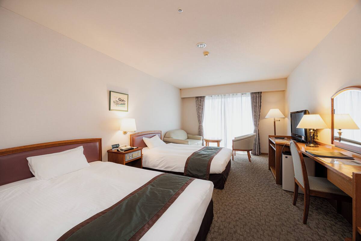 A hotel room with two beds, a desk, a chair, a television, and a small refrigerator.