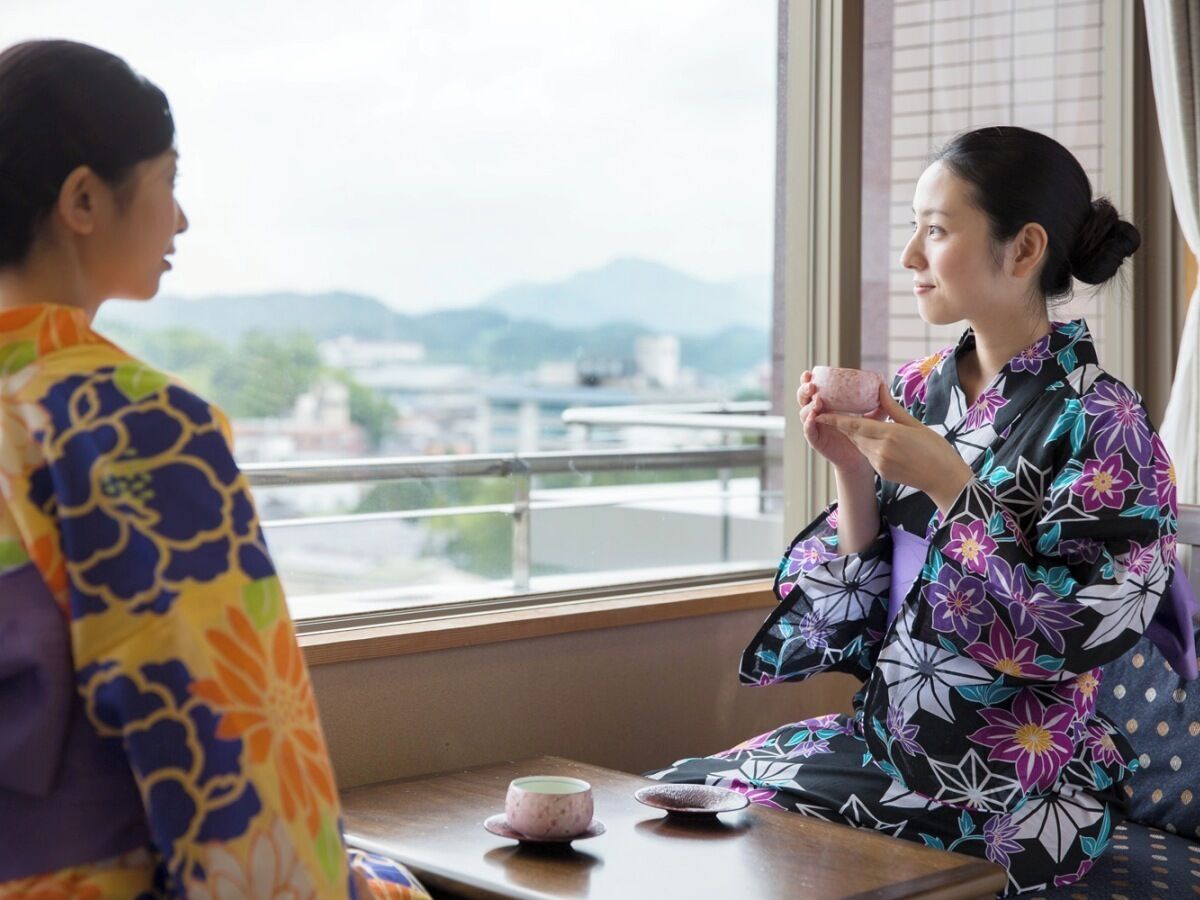 Two individuals in traditional attire sitting at a table with a view of a cityscape through a window.