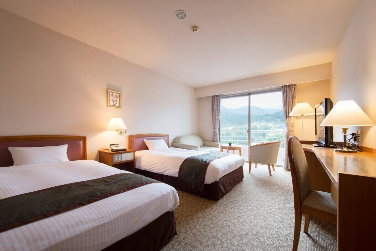 A hotel room with two beds, a desk, a chair, and a view of the mountains.