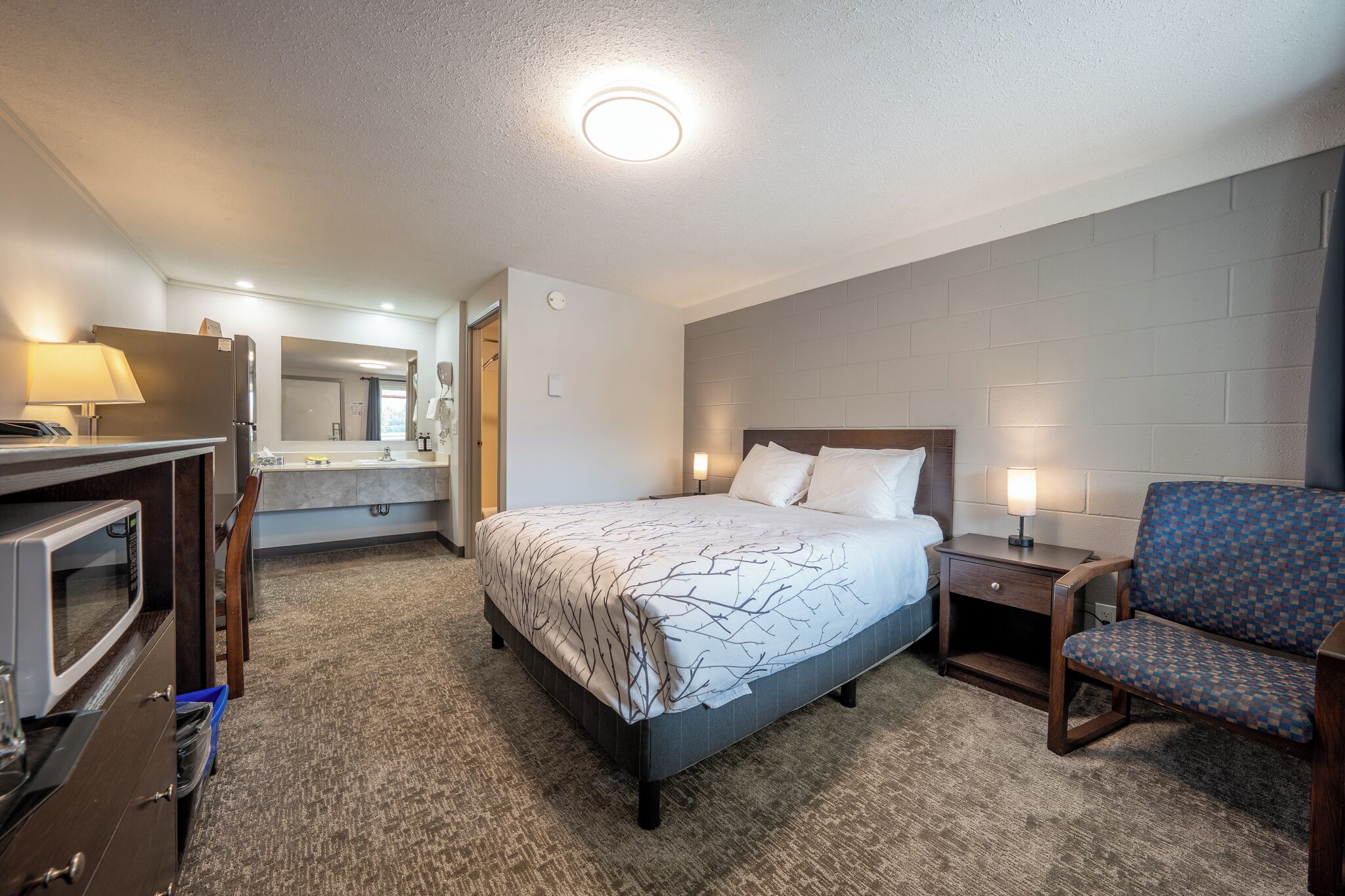 A hotel room with a bed, a desk, a chair, a TV, and a bathroom visible in the background.