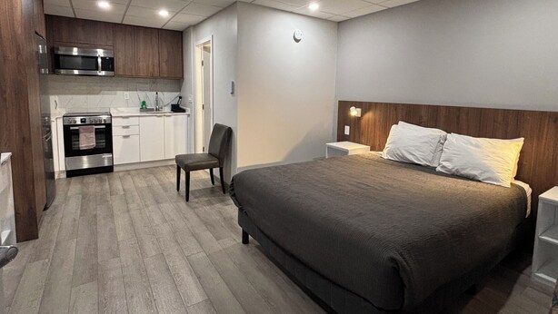 A modern hotel room with a kitchenette, a bed with white linens, and a wooden headboard. - Western Traveller Motel (Grand Forks)