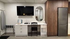 A modern room with a flat-screen TV, a wooden cabinet, a refrigerator, a desk with drawers, a chair, and a mirror. - Western Traveller Motel (Grand Forks)