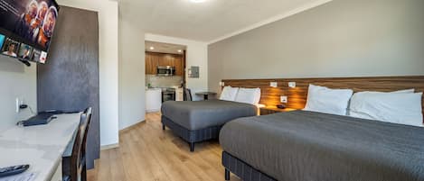 Habitación de hotel con dos camas, un escritorio, una silla, un televisor y una kitchenette al fondo.