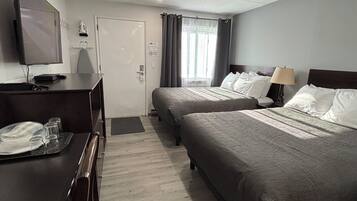 Habitación de hotel con dos camas, un escritorio con televisor y una ventana con cortinas.