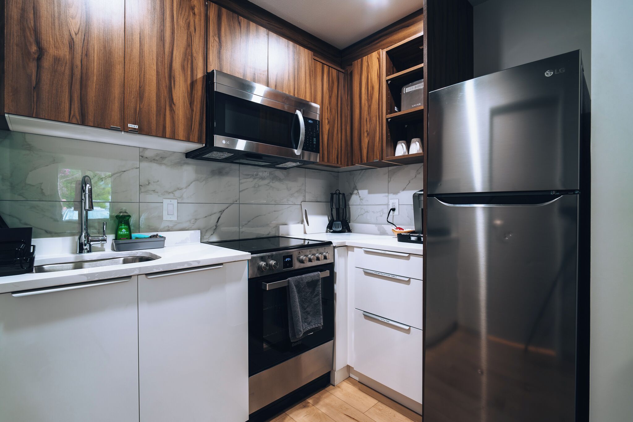 Una cocina con armarios de madera, un microondas de acero inoxidable, un horno y un refrigerador.