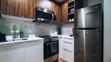 Una cocina con armarios de madera, un microondas de acero inoxidable, un horno y un refrigerador.