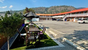 Un motel con mesas al aire libre, estacionamiento y vistas de una cadena montañosa.