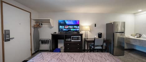 A hotel room with a bed, a desk with a TV, a microwave, a refrigerator, and a small kitchenette.