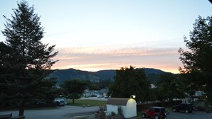 A parking lot with several cars, a small white building with a lit lamp, and a mountain range in the background. - Western Traveller Motel (Grand Forks)