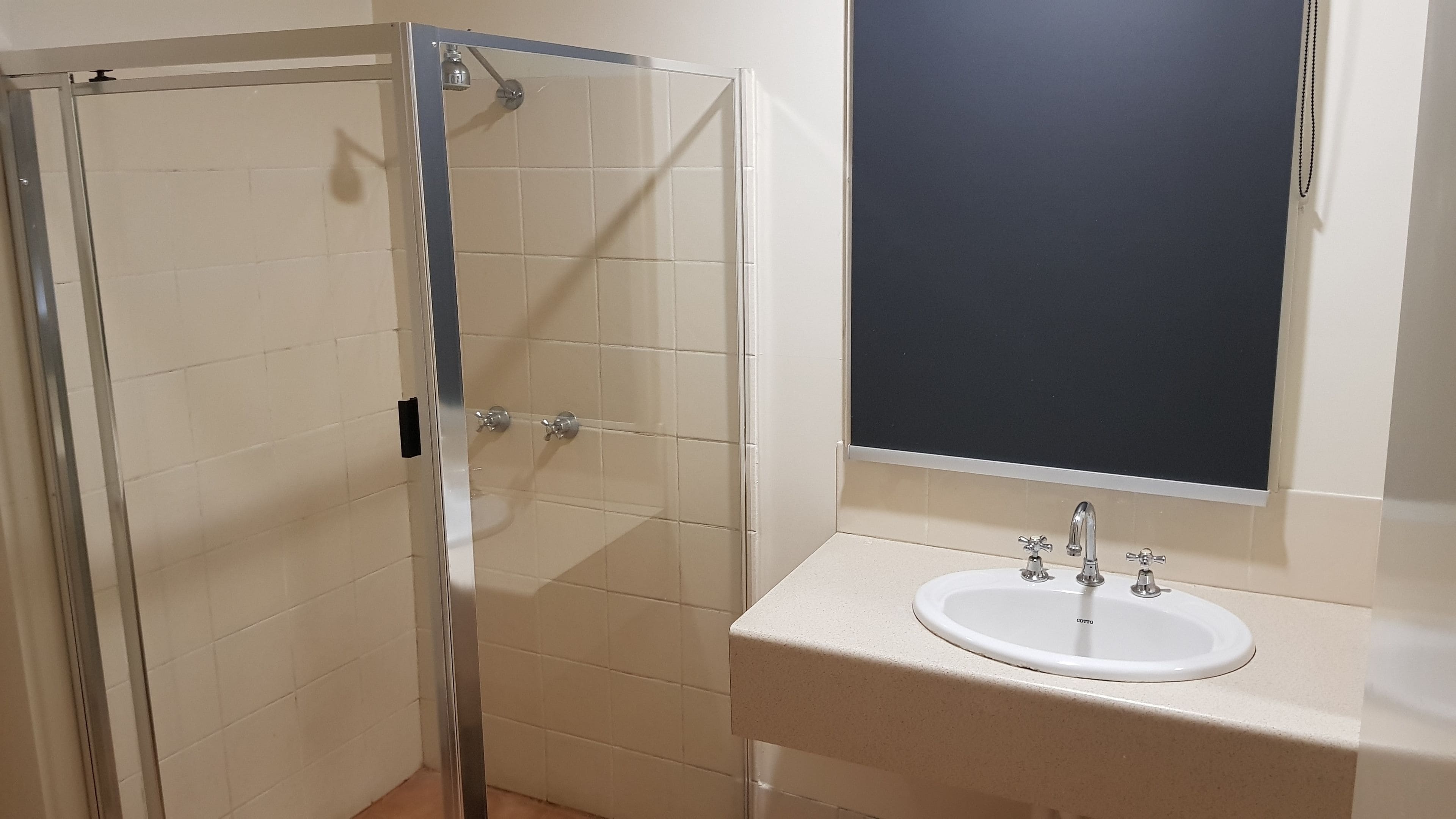 Un baño con cabina de ducha de vidrio, un lavamanos blanco con espejo y paredes de azulejos color beige.