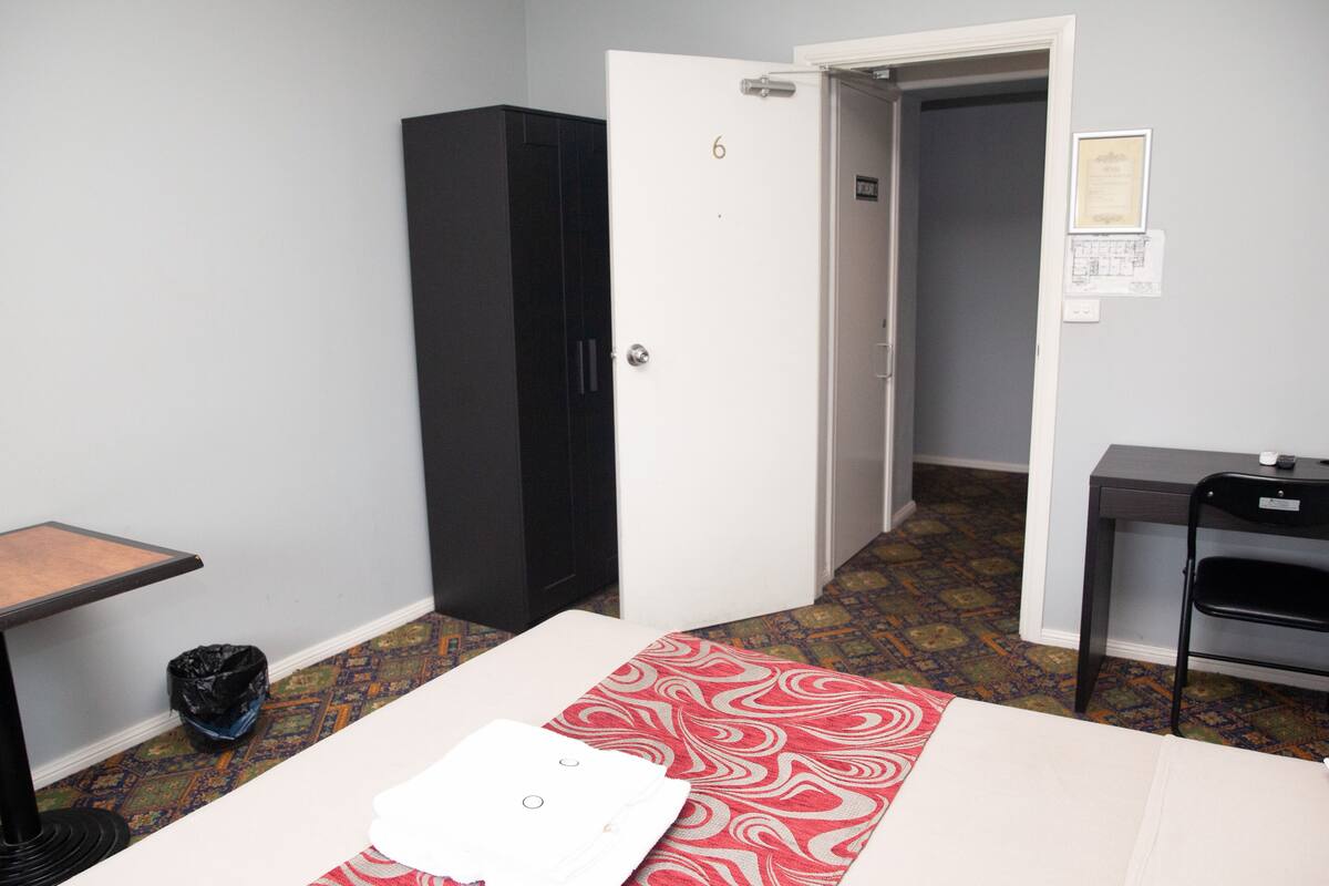 A hotel room with a bed, a desk, a wardrobe, and a door leading to another room.