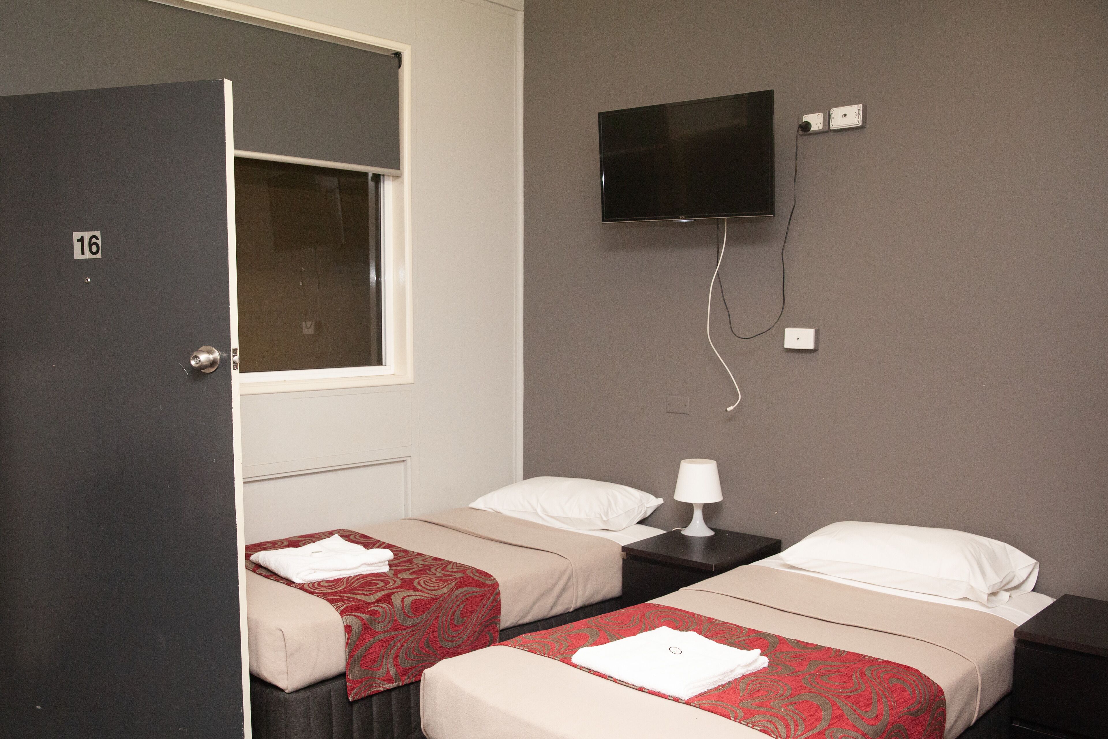 A hotel room with two beds, a TV mounted on the wall, and a door with a number.