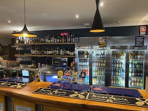 A bar area with a counter, multiple taps, and a digital clock displaying 10:40. - Royal Hotel Singleton (Singleton)