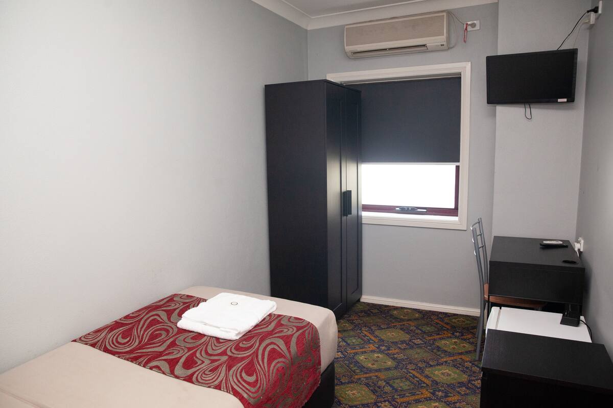A small, simple room with a bed, a desk, a chair, and a TV.