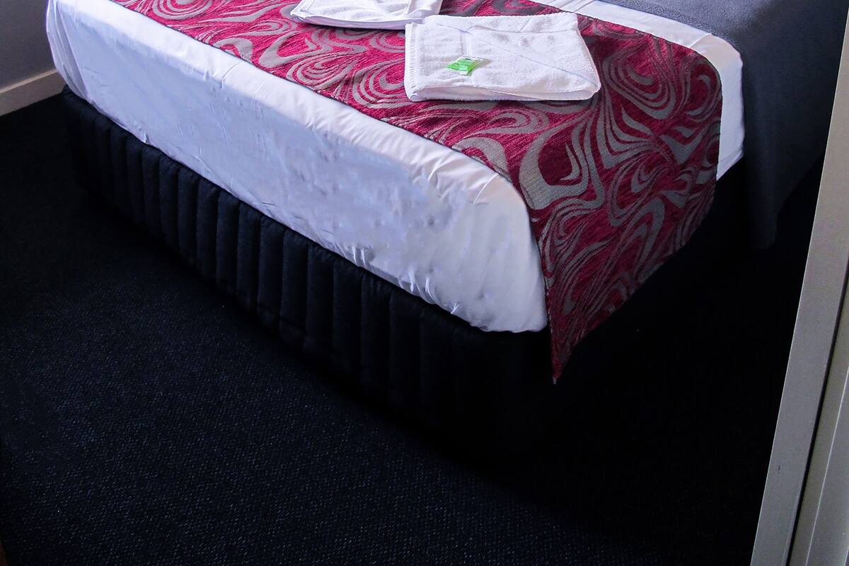 A hotel room with a bed, a nightstand, a lamp, and a window.