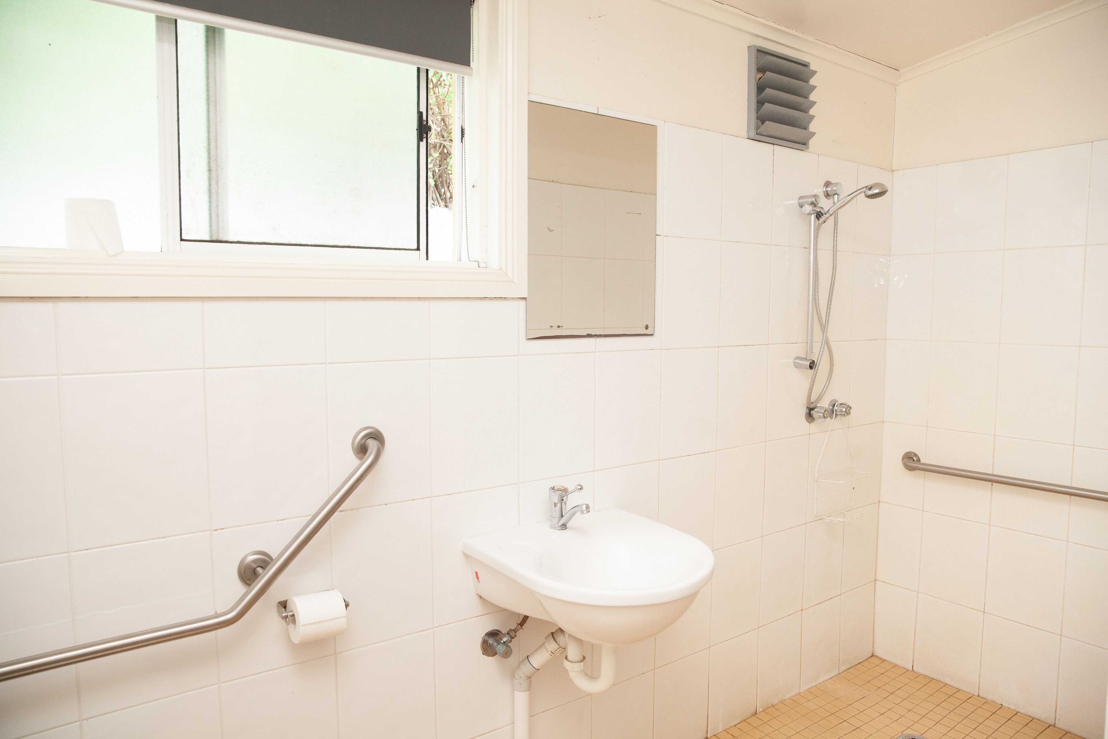 A bathroom with a sink, a mirror, a window, and a shower.