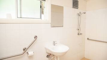 A bathroom with a sink, a mirror, a window, and a shower.