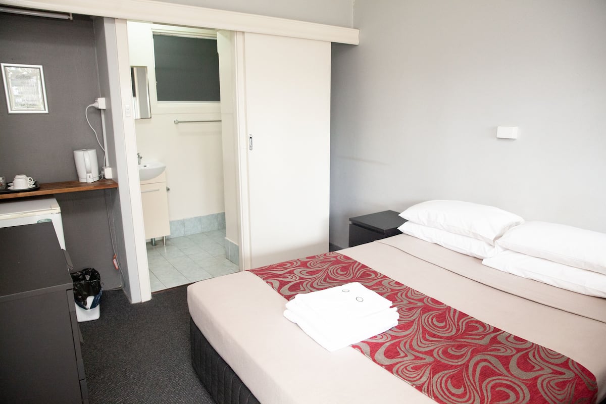 A hotel room with a bed, a desk, a chair, a sink, and a mirror.