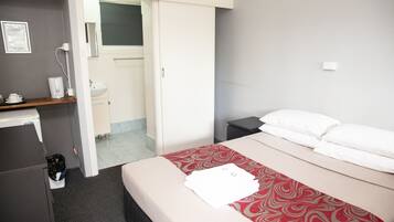 A hotel room with a bed, a desk, a chair, a sink, and a mirror.