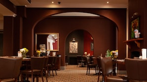 A hotel dining area with a patterned carpet, wooden chairs, tables, and an arched ceiling. - Royal Hotel Singleton (Singleton)