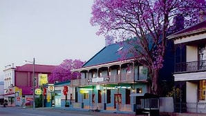 A street view with a building featuring a balcony and a tree with purple flowers. - Royal Hotel Singleton (Singleton)