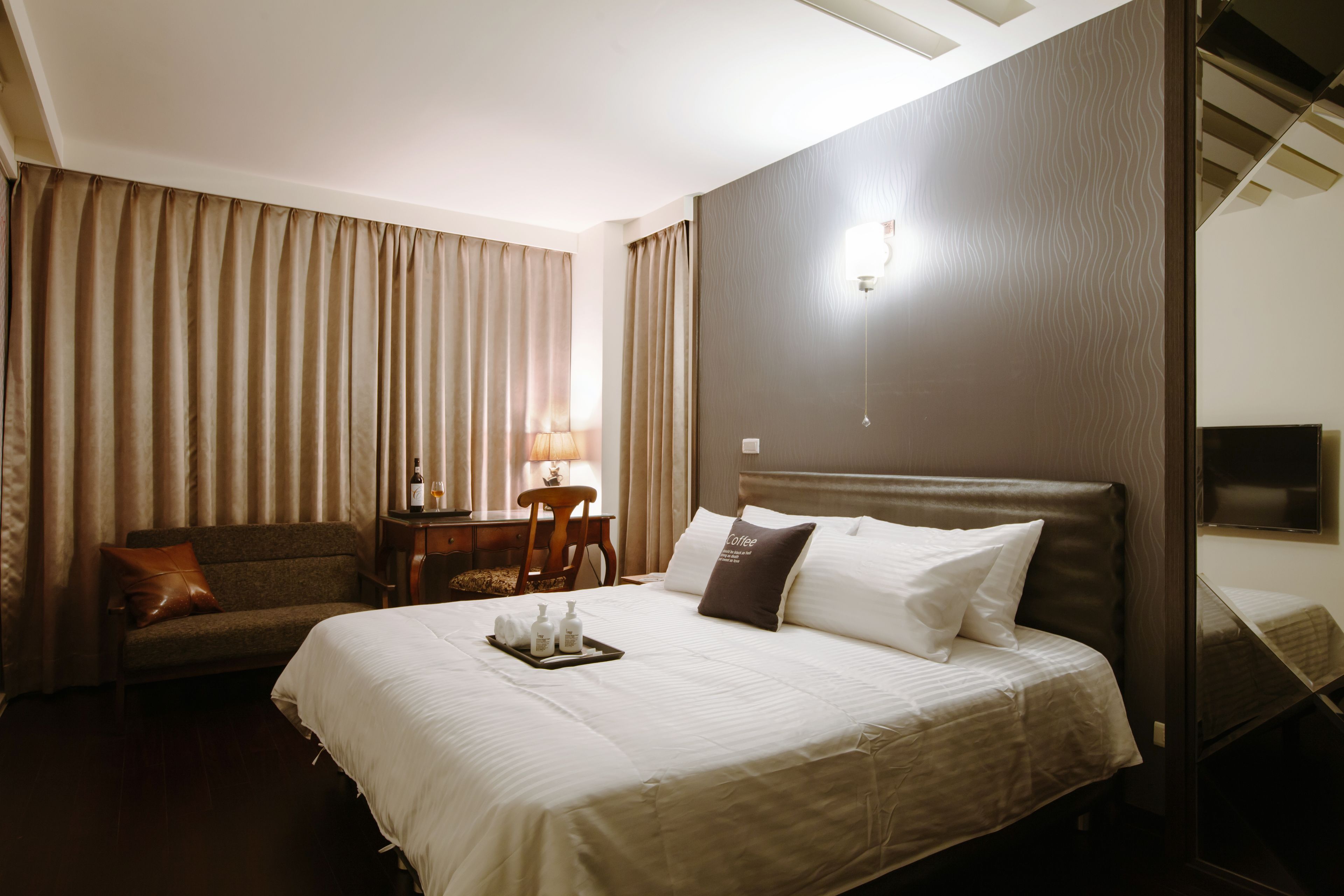 A hotel room with a large bed, a sofa, a desk with a lamp, and a window with curtains.