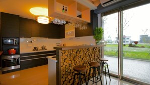 A modern kitchen with a central island, bar stools, and a view of the outdoors through large windows. - Grand Allevia Villa (Wujie)