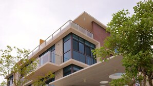 A modern multi-story building with a covered entrance, outdoor seating, and greenery. - Grand Allevia Villa (Wujie)