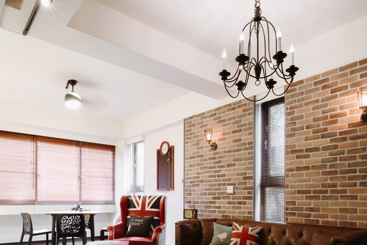 A modern living room with a brick wall, leather sofa, and a chandelier.