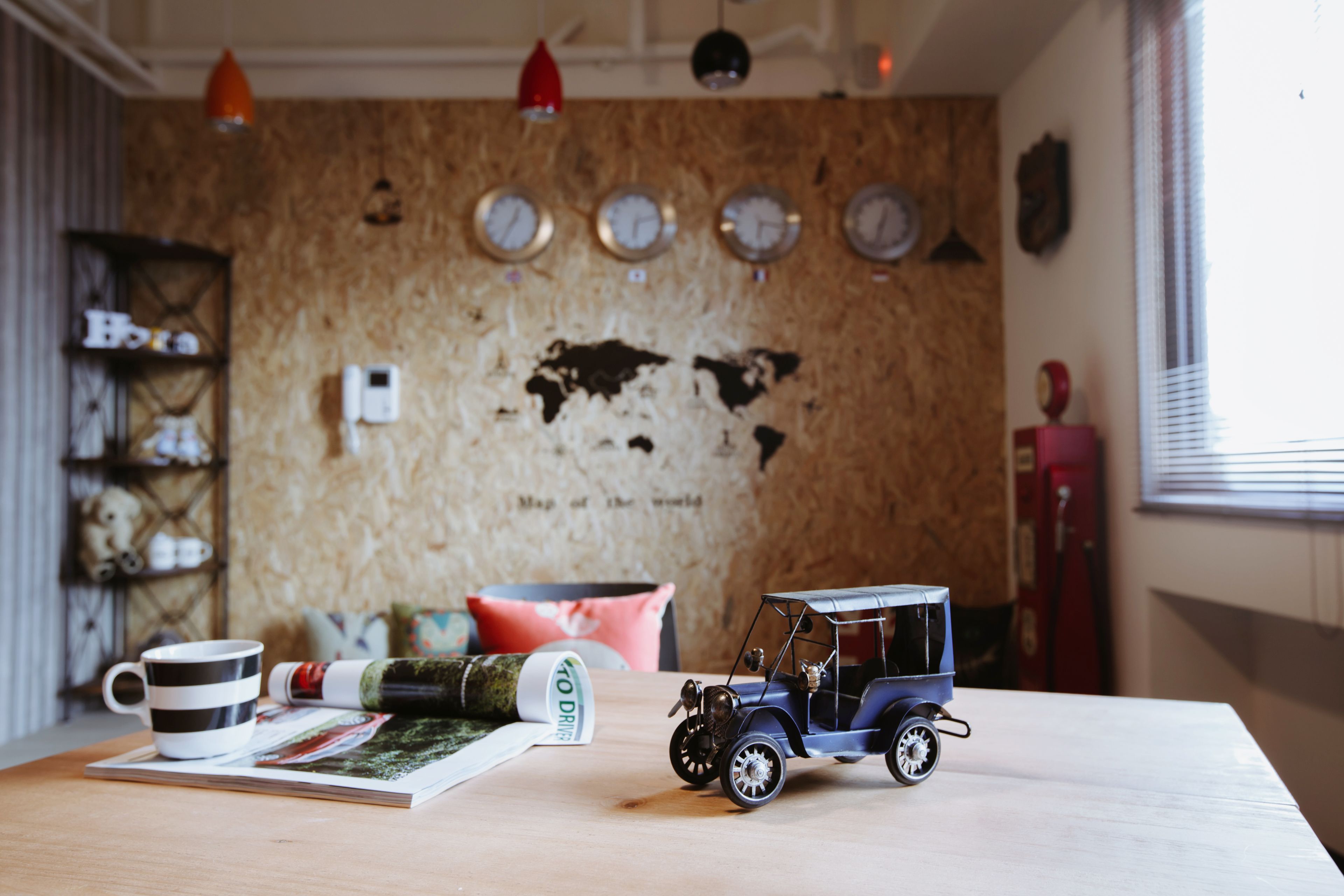 A room with a wooden wall, a small table with a toy car, a mug, and a rolled-up magazine.