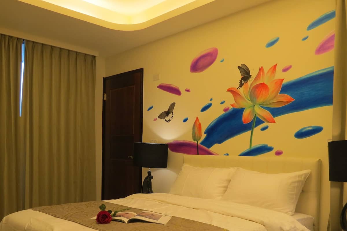 A hotel room with a bed, a nightstand, a lamp, and a wall with a floral mural.