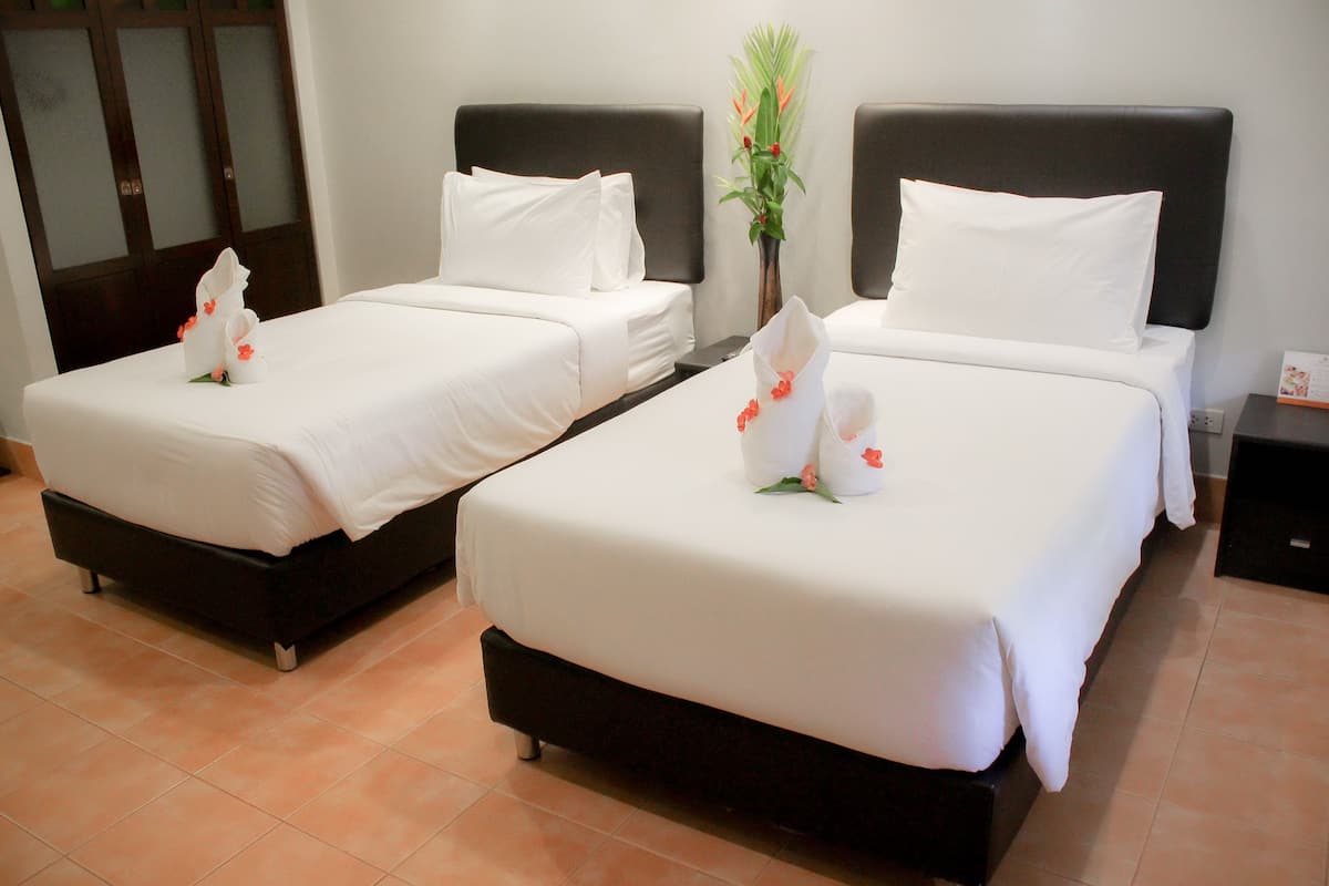Two neatly made beds with white linens and decorative flower arrangements, a dark headboard, and a tiled floor.
